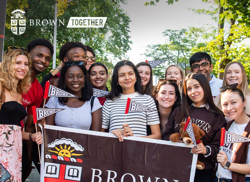 Incoming students holding a Brown banner on a sunny day.