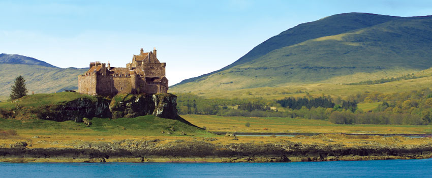 Castle near water in Scothland with rolling, green hills in the background