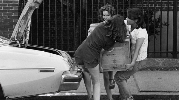 Three Brown University students loading a wooden crate into a trunk of a car.