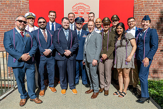 RI Senator Jack Reed posing with five 2023 Brown ROTC graduates in front of flags