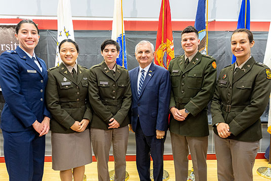 RI Senator Jack Reed posing with five 2023 Brown ROTC graduates in front of flags