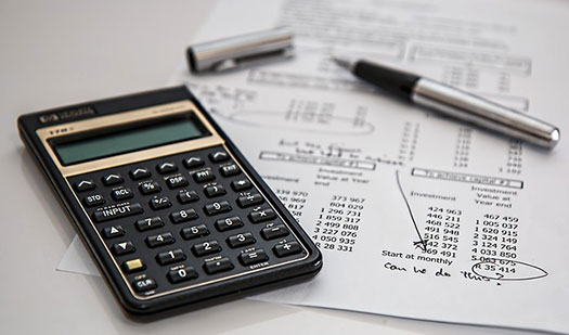 calculator and pen on top of sheet showing financial data